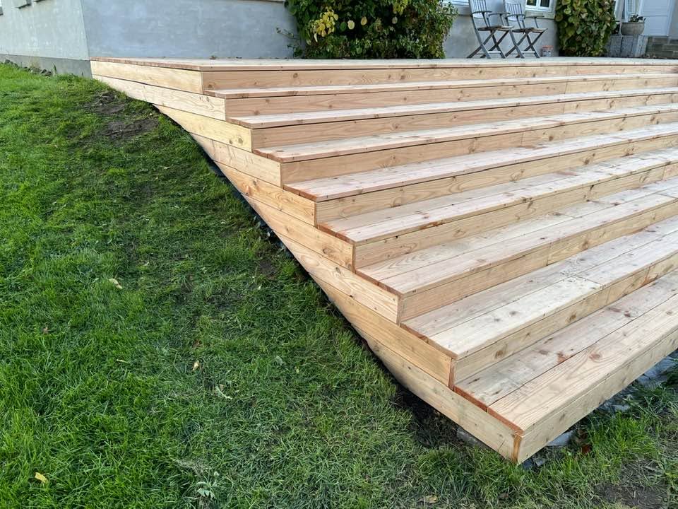 Bred trappe i lærketræ ned til græsplænen som del af terrasseprojekt